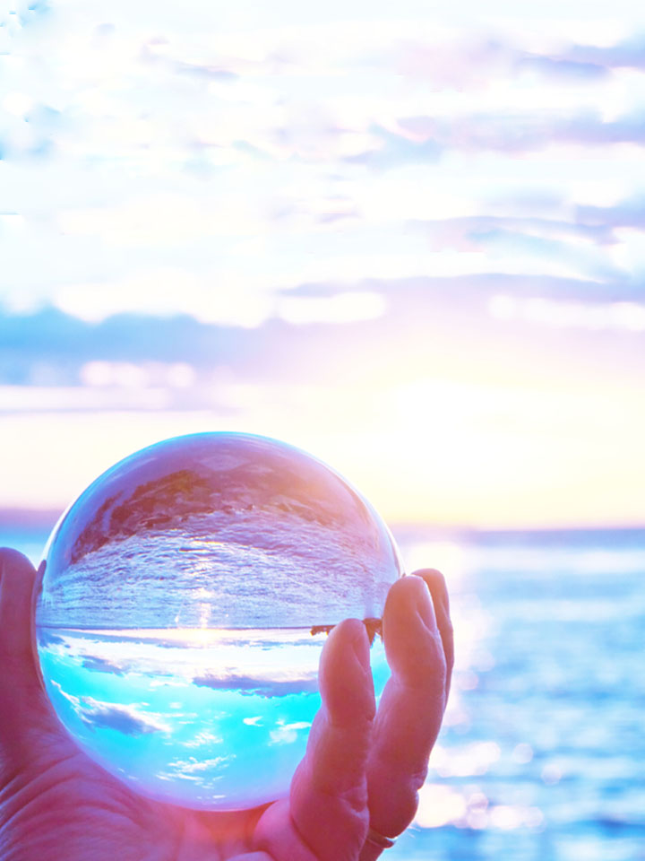A person holding a glass ball in front of the ocean.